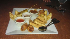 Chicken satay (upper left), fried tofu (bottom right), crab Rangoon (left and right), spring rolls (upper right and bottom), and three sauces (from left to right: sweet and sour, cucumber, and peanut)