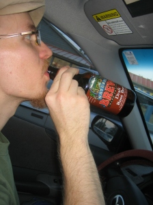 Erik, drinking a bottle of "Natural Brew Hand Crafted Draft Root Beer" outside of Bloomingfoods