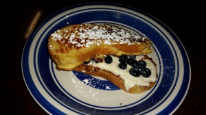 Two thick slabs of French toast with powdered sugar on top and cream cheese and blueberries in between.